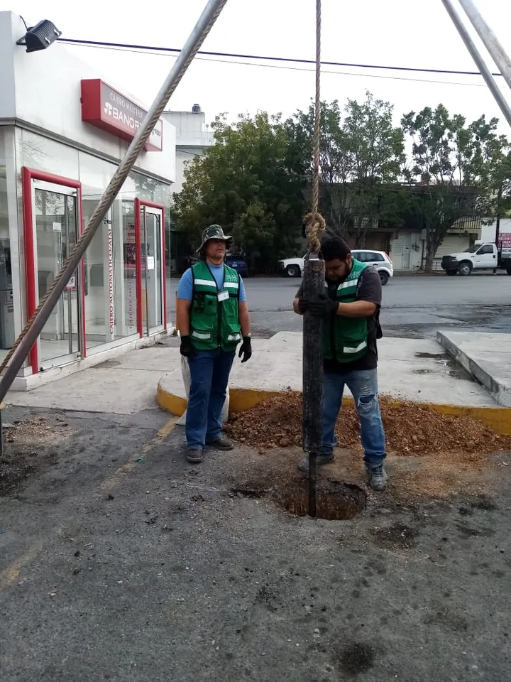 Dos técnicos con chaleco verde haciendo un sondeo manual de suelo en un predio urbano